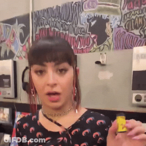 A Woman Is Holding A Small Yellow Object In Front Of A Wall With Graffiti On It That Says ' I Love You ' GIF