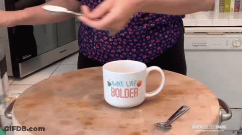 A Woman Is Holding A Spoon Over A Mug That Says Make Life Bolder GIF