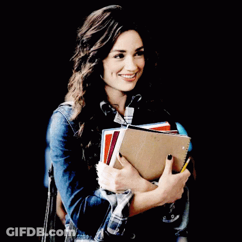 A Woman Is Holding A Stack Of Books And Smiling GIF
