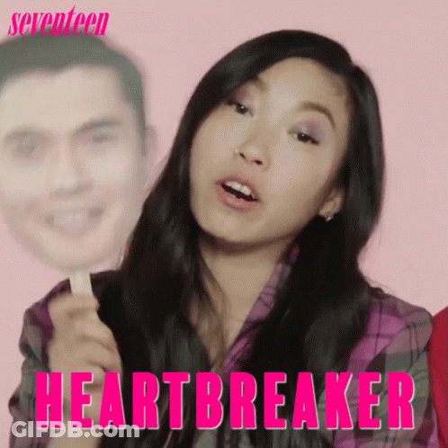 A Woman Is Holding A Stick With A Picture Of A Man On It And The Words Heartbreaker Written On It GIF