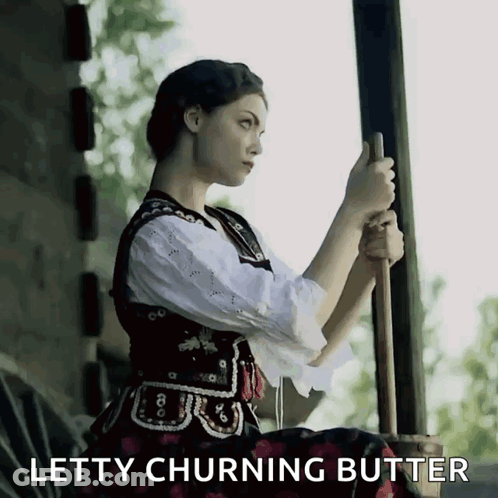 A Woman Is Holding A Stick With The Words Letty Churning Butter Behind Her GIF