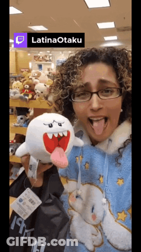 A Woman Is Holding A Stuffed Animal In Front Of A Sign That Reads Latinaotaku GIF