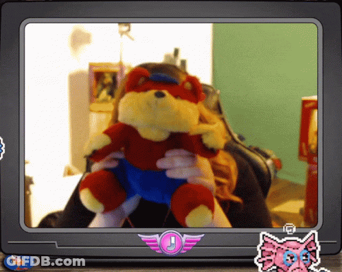A Woman Is Holding A Stuffed Animal In Front Of A Tv Screen With A Sticker That Says J GIF