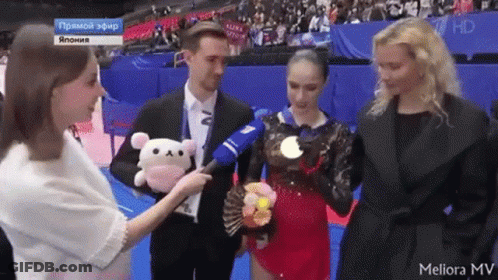 A Woman Is Holding A Stuffed Animal While Talking To A Man And A Woman GIF