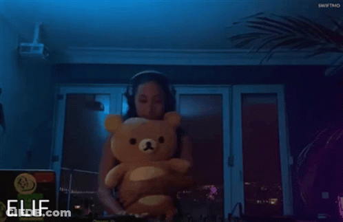 A Woman Is Holding A Teddy Bear In Front Of A Sign That Says Elif GIF