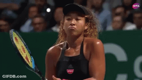 A Woman Is Holding A Tennis Racquet And Making A Face . GIF