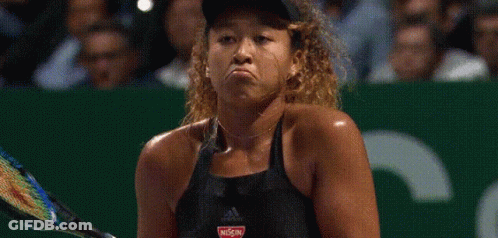 A Woman Is Holding A Tennis Racquet And Making A Funny Face While Playing Tennis . GIF