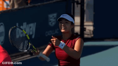 A Woman Is Holding A Tennis Racquet And Smiling . GIF