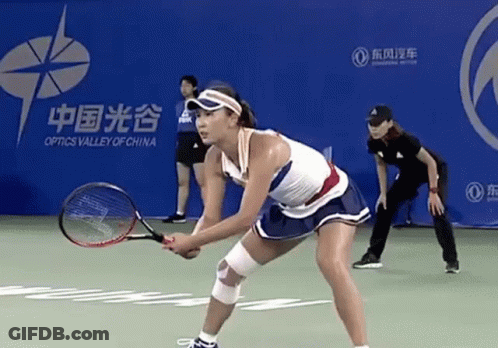 A Woman Is Holding A Tennis Racquet On A Court In Front Of An Optics Valley Of China Banner GIF