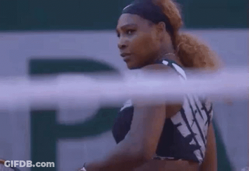 A Woman Is Holding A Tennis Racquet On A Tennis Court And Looking At The Camera . GIF