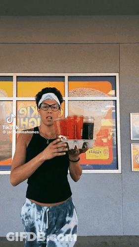 A Woman Is Holding A Tray Of Food In Front Of A Window With A Sign That Says ' Ok Hot ' On It GIF