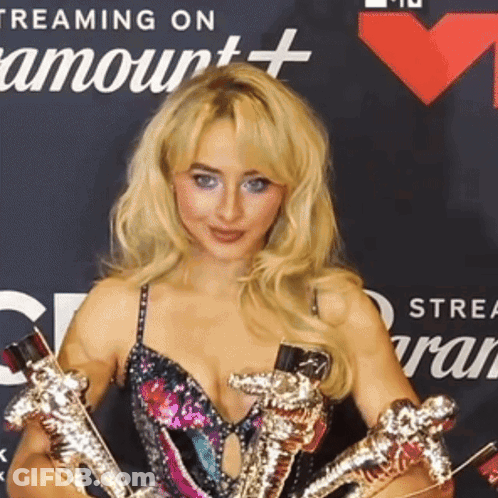 A Woman Is Holding A Trophy In Front Of A Banner That Says Streaming On Amour + GIF