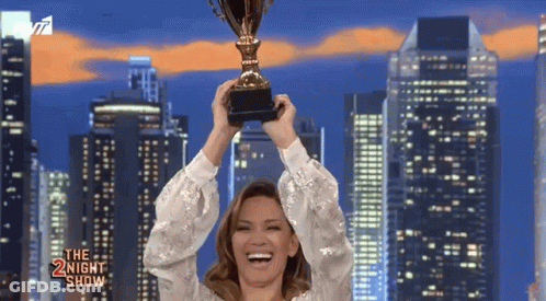 A Woman Is Holding A Trophy In Front Of A City Skyline And The Words The Night Show Are On The Bottom GIF