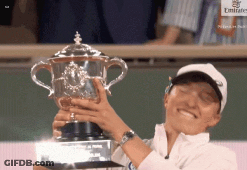 A Woman Is Holding A Trophy In Front Of A Emirates Sign GIF