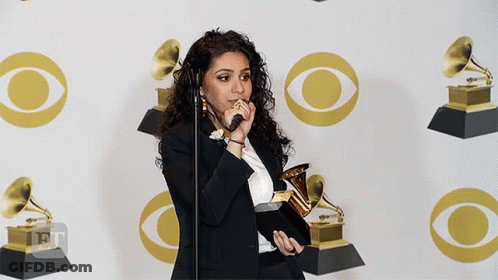 A Woman Is Holding A Trophy In Front Of A Wall With Cbs Logos GIF