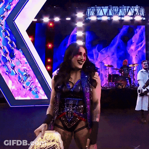 A Woman Is Holding A Trophy On A Stage With A Band Behind Her GIF