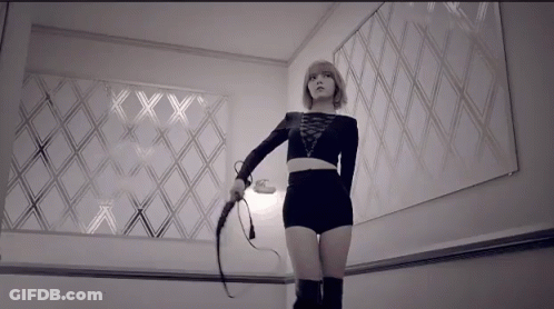 A Woman Is Holding A Whip In Front Of A Wall With The Letters Xx On It GIF