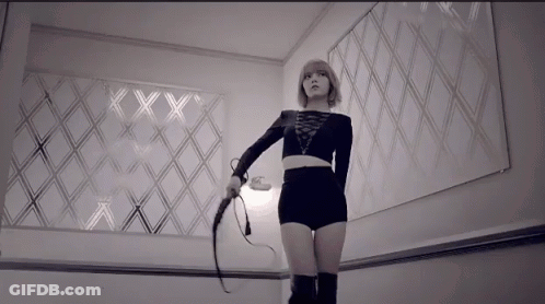 A Woman Is Holding A Whip In Front Of A Wall With The Letters Xx On It GIF