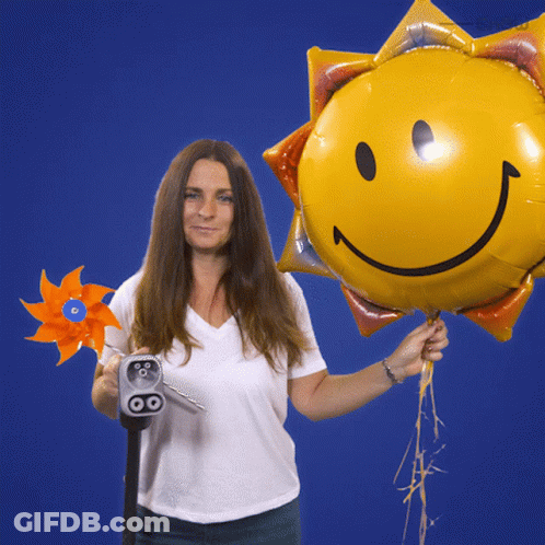 A Woman Is Holding A Windmill And A Balloon With A Smiley Face On It GIF