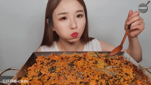 A Woman Is Holding A Wooden Spoon Over A Pan Of Food With The Name Hamzy On The Bottom GIF
