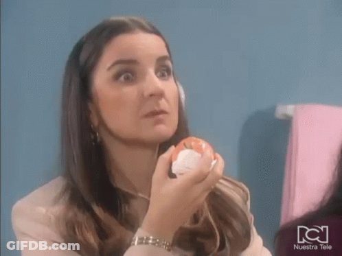 A Woman Is Holding An Apple In Her Hand In Front Of Her Face . GIF