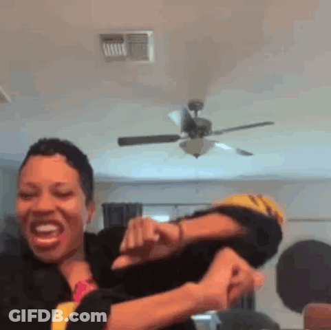 A Woman Is Holding Another Woman 'S Arm In A Room With A Ceiling Fan . GIF