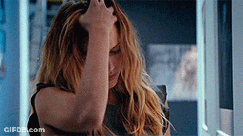 A Woman Is Holding Her Head With Her Hand While Looking At Herself In The Mirror . GIF