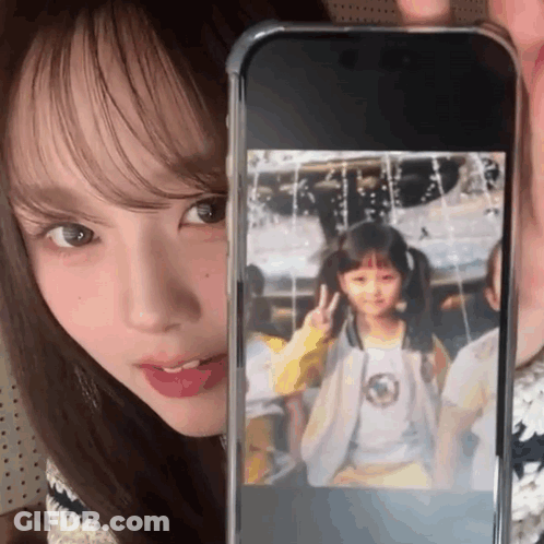 A Woman Is Holding Up A Cell Phone With A Picture Of A Young Girl On It GIF