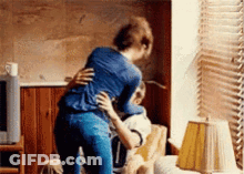 A Woman Is Hugging A Man In A Living Room . GIF