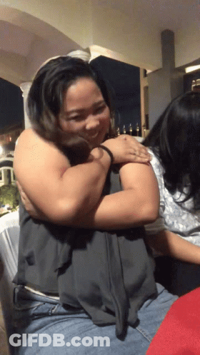 A Woman Is Hugging Another Woman In A Dark Room At Night GIF