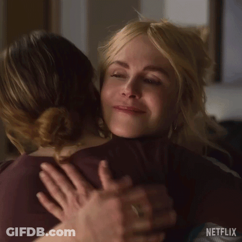 A Woman Is Hugging Another Woman In A Room . GIF