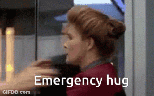 A Woman Is Hugging Another Woman With The Words `` Emergency Hug '' Written On The Bottom Of The Image . GIF