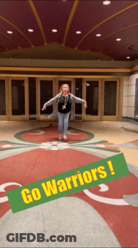 A Woman Is Jumping In Front Of A Building With A Sign That Says Go Warriors GIF