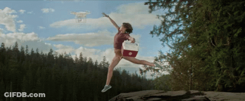 A Woman Is Jumping In The Air With A Cooler And A Drone In The Background GIF
