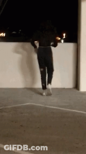 A Woman Is Jumping Over A Wall In A Parking Lot . GIF