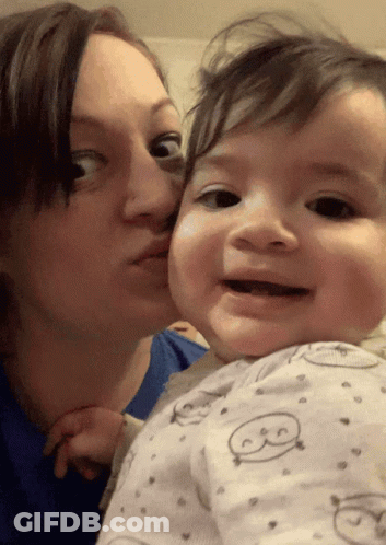 A Woman Is Kissing A Baby On The Cheek Who Is Wearing A Pajama With The Letter B On It GIF