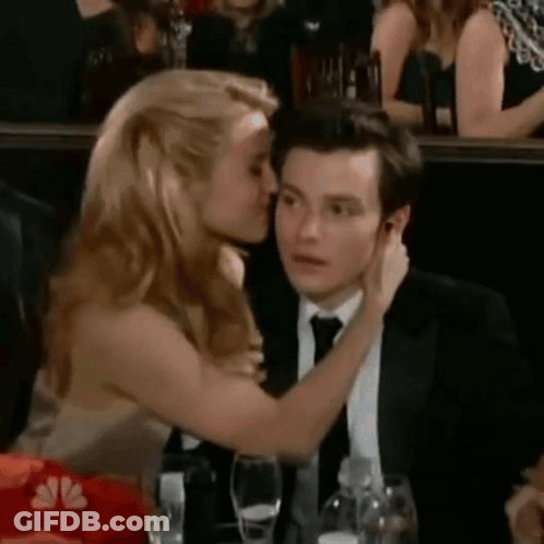 A Woman Is Kissing A Man On The Cheek In A Crowd Of People . GIF