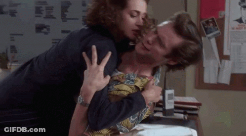 A Woman Is Kissing A Man On The Cheek In A Room . GIF