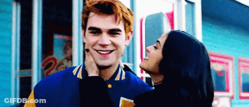 A Woman Is Kissing A Man On The Cheek While They Are Standing In Front Of A Building . GIF