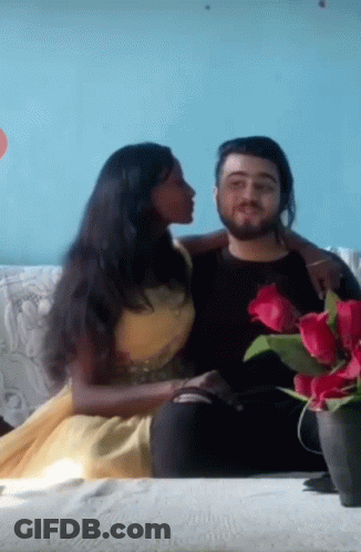 A Woman Is Kissing A Man On The Cheek While They Sit On A Couch GIF
