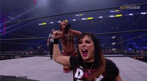 A Woman Is Kneeling Down In A Wrestling Ring While Another Woman Holds Her Fist Up In The Air . GIF