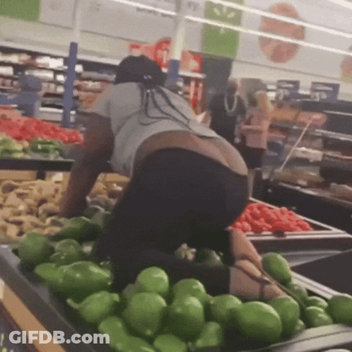 A Woman Is Kneeling Down In Front Of A Bunch Of Green Peppers In A Grocery Store GIF