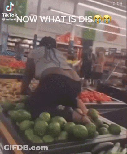 A Woman Is Kneeling Down In Front Of A Tray Of Green Peppers . GIF