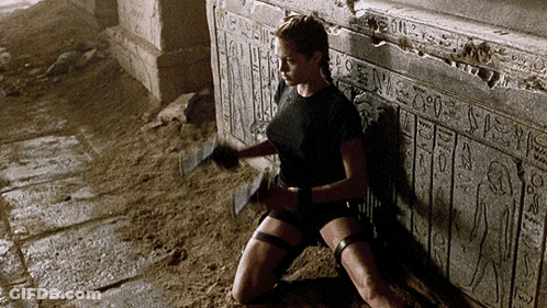 A Woman Is Kneeling Down In Front Of A Wall That Says Egyptian Hieroglyphics GIF