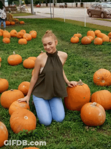 A Woman Is Kneeling In A Field Of Pumpkins And Smiling GIF