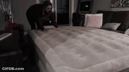 A Woman Is Kneeling On A Mattress In A Dark Room GIF