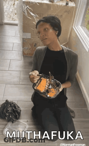 A Woman Is Kneeling On The Floor Holding A Container Of Food That Says Muthafuka On The Bottom GIF