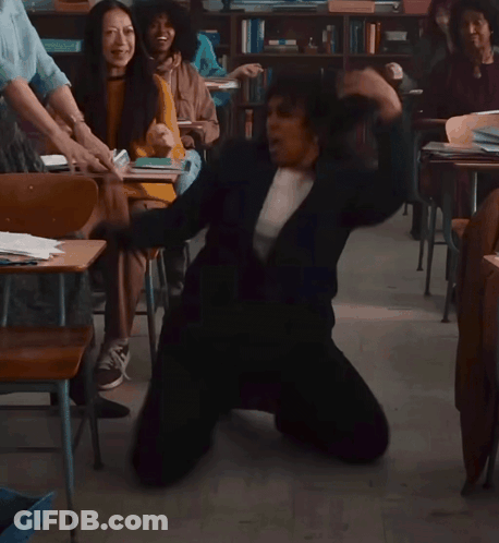 A Woman Is Kneeling On The Floor In A Classroom With Other People GIF
