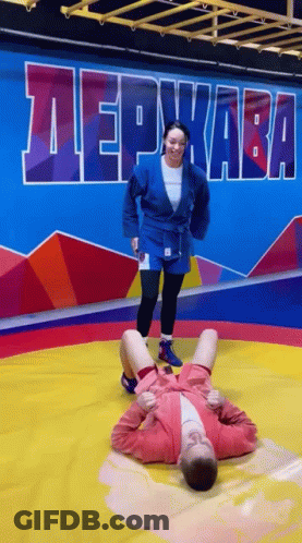 A Woman Is Kneeling On Top Of A Man On A Wrestling Mat In A Gym . GIF