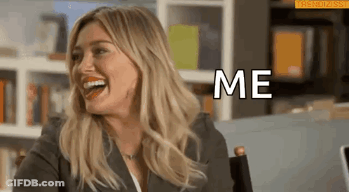 A Woman Is Laughing And Saying `` Me '' While Sitting In Front Of A Bookshelf . GIF